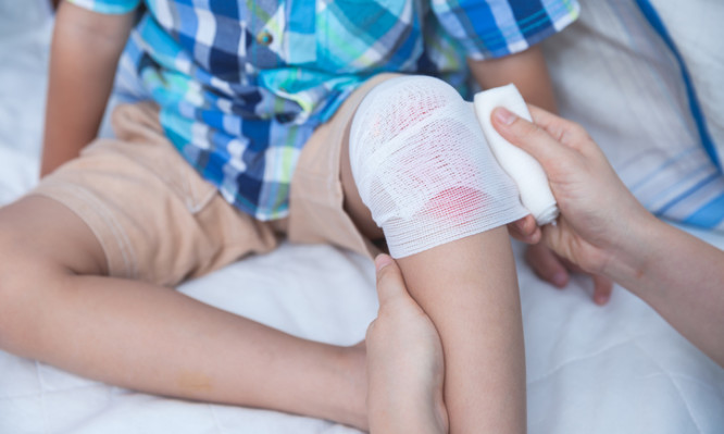 Child injured. Mother bandaging son's knee, bandage in focus. Human health care and medicine concept.