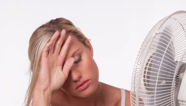 A young woman sits in front of a fan to cool off in a heatwave.