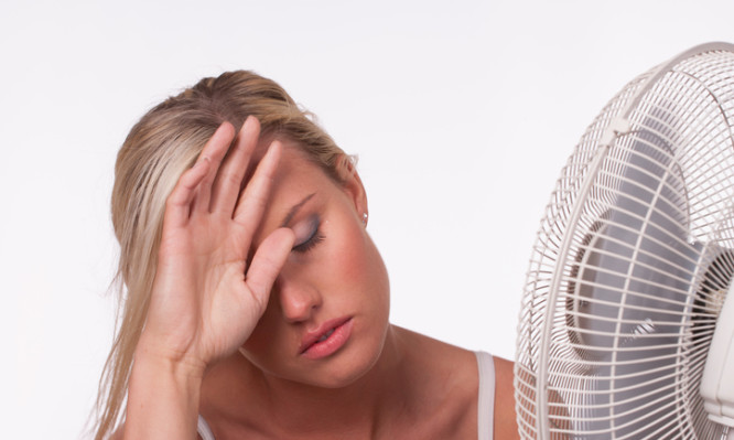 A young woman sits in front of a fan to cool off in a heatwave.