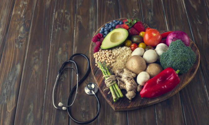 Healthy food on a heart shape cutting board. Love of food concept with fruit, vegetables, grains and high fibre foods. Rustic wood textures. There is also a stethoscope
