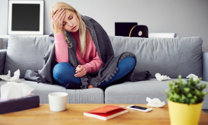 Sick woman with headache sitting under the blanket in living room