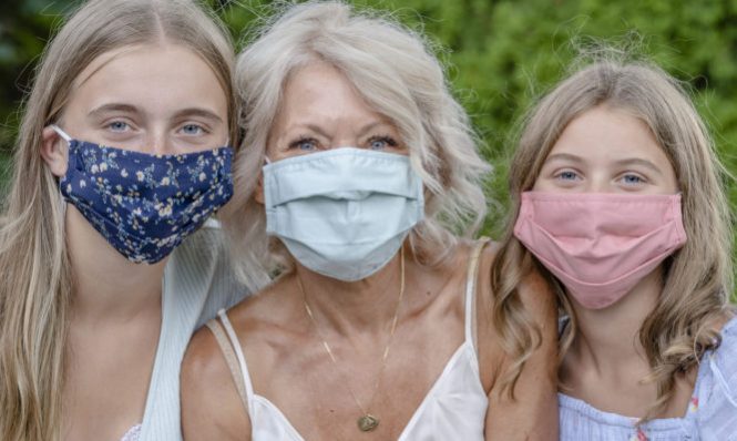Close up of grandmother sitting with her two granddaughters wearing protective face masks to avoid the spread of COVID-19.