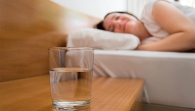 woman lying on bed with closeup of glass of  mineral water on the nightstand