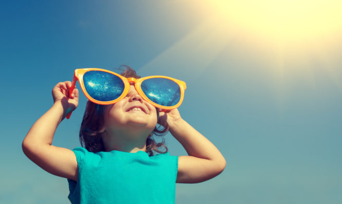 Happy little girl with big sunglasses looking at the sun