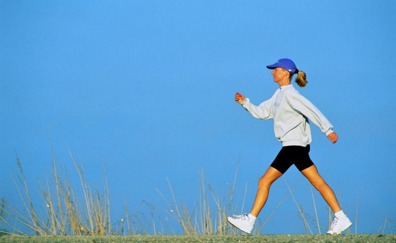 Woman speed walking, profile, against blue sky