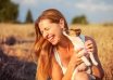 Young woman holding Jack Russell terrier puppy on her hand, trying to pose, but the dog is licking and chewing her ear and hair.