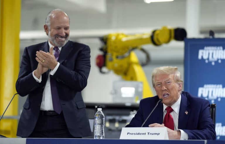 Republican presidential nominee former President Donald Trump arrives for a roundtable, Friday, Oct. 18, 2024, in Auburn Hills, Mich.,as Howard Lutnick, CEO of Cantor Fitzgerald applauds. (AP Photo/Evan Vucci)